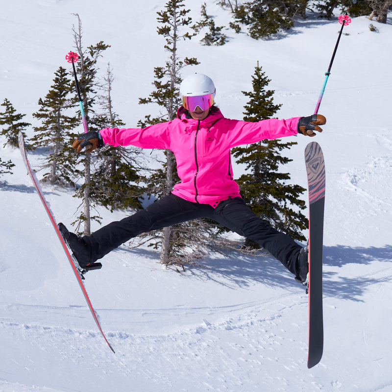 | big_air.JPG | A skier jumps mid-air in a snowy mountain setting, wearing a bright pink ski jacket, black ski pants, a white helmet, and pink-tinted goggles, with ski poles and skis extended.