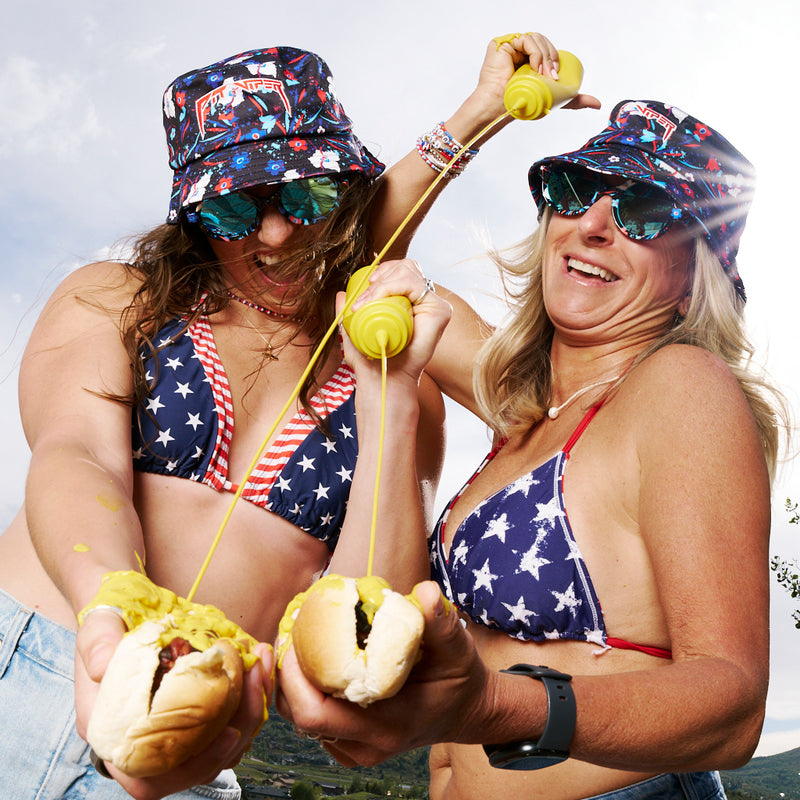 | macuga_fam.jpg | Two women in patriotic outfits holding hot dogs with mustard, wearing sunglasses and hats.